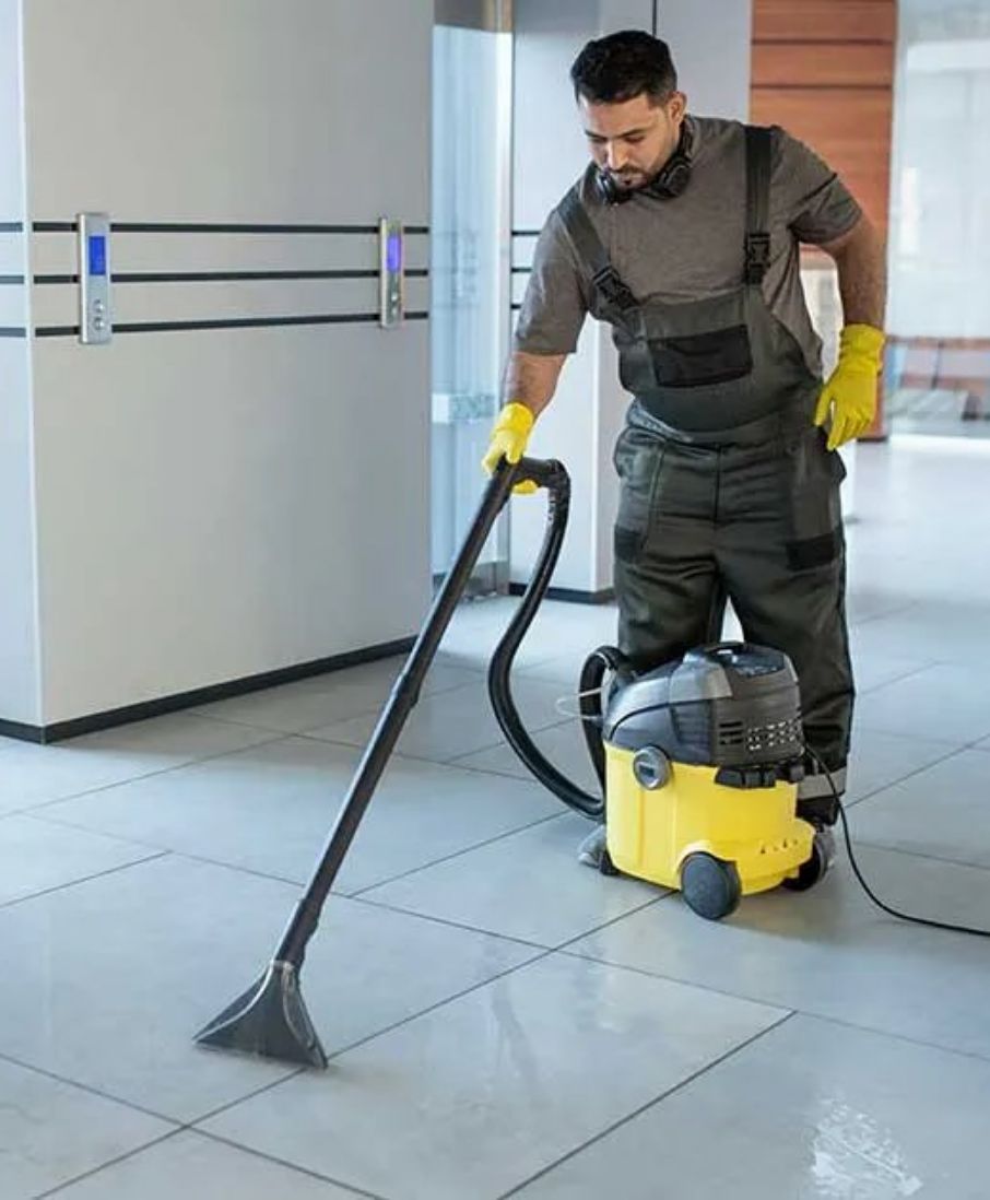 Cleaner vacuuming a carpeted office floor.